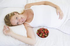 Zwangere vrouw die in bed met kom fruit ligt royalty-vrije stock foto's Zwangere vrouw die in bed met kom fruit ligt royalty-vrije stock foto's