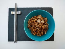 Zwarte leibasis met blauwe kom van kekers met tofu en ui met metaaleetstokjes op witte achtergrond stock fotografie Zwarte leibasis met blauwe kom van kekers met tofu en ui met metaaleetstokjes op witte achtergrond stock fotografie