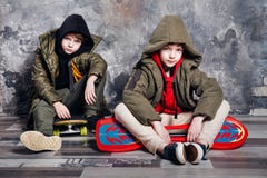 Zwei kleine Doppeljungen in der zufälligen Kleidung, die auf Skateboard im Studio sitzt Jugendlich und Kindermodekonzept lizenzfreie stockbilder Zwei kleine Doppeljungen in der zufälligen Kleidung, die auf Skateboard im Studio sitzt Jugendlich und Kindermodekonzept lizenzfreie stockbilder