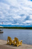Zwei leere hölzerne Adirondack-Stühle oder Muskoka-deckchairs auf dem hölzernen Ufer, das szenischen ruhigen Fluss übersieht stockfotos Zwei leere hölzerne Adirondack-Stühle oder Muskoka-deckchairs auf dem hölzernen Ufer, das szenischen ruhigen Fluss übersieht stockfotos