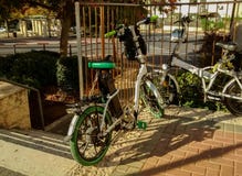 Zwei Paare Fahrräder - eine von ihnen elektrisch, angekettet, um Zaun, nahe Schritte zu asphaltieren, die unten zur Straße gehen lizenzfreie stockbilder Zwei Paare Fahrräder - eine von ihnen elektrisch, angekettet, um Zaun, nahe Schritte zu asphaltieren, die unten zur Straße gehen lizenzfreie stockbilder