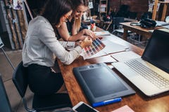 Zwei weibliche Architekten, die unter Verwendung der Farbmuster sitzen am Schreibtisch mit Laptop, grafische Tablette im Designst Lizenzfreie Stockfotografie Zwei weibliche Architekten, die unter Verwendung der Farbmuster sitzen am Schreibtisch mit Laptop, grafische Tablette im Designst Lizenzfreie Stockfotografie