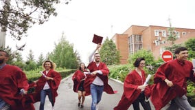 Zwolnione tempo wesoło absolwenci biega, trzyma dyplomy i macha mortarboards cieszy się wolność, dobrej edukacji zbiory wideo Zwolnione tempo wesoło absolwenci biega, trzyma dyplomy i macha mortarboards cieszy się wolność, dobrej edukacji zbiory wideo
