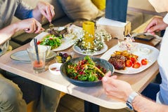 À la table, deux hommes mangent le dîner, mangent d'un bifteck, avec de la salade d'un plat blanc, avec une fourchette et un cout Images libres de droits À la table, deux hommes mangent le dîner, mangent d'un bifteck, avec de la salade d'un plat blanc, avec une fourchette et un cout Images libres de droits
