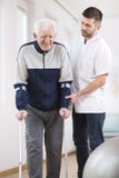 Älterer Mann, der auf Krücken gehen und eine hilfreiche männliche Krankenschwester, die ihn stützt stockbilder Älterer Mann, der auf Krücken gehen und eine hilfreiche männliche Krankenschwester, die ihn stützt stockbilder