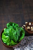 Épinards frais avec les raisins secs, pignons dans une cuvette en bois sur le fond en bois rustique, foyer sélectif image stock Épinards frais avec les raisins secs, pignons dans une cuvette en bois sur le fond en bois rustique, foyer sélectif image stock
