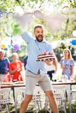 Équipez sauter avec un gâteau sur une célébration de famille ou une réception en plein air dehors photo stock Équipez sauter avec un gâteau sur une célébration de famille ou une réception en plein air dehors photo stock