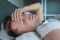 Équipez se situer dans le lit à la maison souffrant du mal de tête ou de la gueule de bois Images stock Équipez se situer dans le lit à la maison souffrant du mal de tête ou de la gueule de bois Images stock