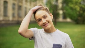 Étudiant de sourire corrigeant la coiffure contre l'université, échange d'étudiants photos stock Étudiant de sourire corrigeant la coiffure contre l'université, échange d'étudiants photos stock