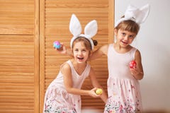 Δύο αστείες μικρές αδελφές στα φορέματα με τα αυτιά του άσπρου κουνελιού στα κεφάλια τους έχουν τη διασκέδαση με τα βαμμένα αυγά στοκ φωτογραφία με δικαίωμα ελεύθερης χρήσης Δύο αστείες μικρές αδελφές στα φορέματα με τα αυτιά του άσπρου κουνελιού στα κεφάλια τους έχουν τη διασκέδαση με τα βαμμένα αυγά στοκ φωτογραφία με δικαίωμα ελεύθερης χρήσης