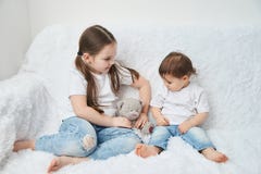 Δύο παιδιά, αδελφές κάθονται σε έναν άσπρο καναπέ στις άσπρα μπλούζες και το τζιν παντελόνι Το μαλακό βελούδο αντέχει στοκ εικόνα με δικαίωμα ελεύθερης χρήσης Δύο παιδιά, αδελφές κάθονται σε έναν άσπρο καναπέ στις άσπρα μπλούζες και το τζιν παντελόνι Το μαλακό βελούδο αντέχει στοκ εικόνα με δικαίωμα ελεύθερης χρήσης