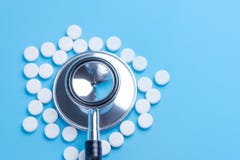 Άσπρες χάπια ή ταμπλέτες και στηθοσκόπιο στο μπλε υπόβαθρο στοκ εικόνες Άσπρες χάπια ή ταμπλέτες και στηθοσκόπιο στο μπλε υπόβαθρο στοκ εικόνες