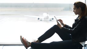 Γυναίκα χρησιμοποιώντας τη σύγχρονη ταμπλέτα υπό εξέταση και καθμένος στο termina αερολιμένων απόθεμα βίντεο Γυναίκα χρησιμοποιώντας τη σύγχρονη ταμπλέτα υπό εξέταση και καθμένος στο termina αερολιμένων απόθεμα βίντεο