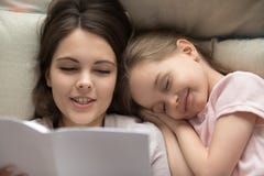 Ευτυχές μικρό κορίτσι που πέφτει κοιμισμένο στο βιβλίο ανάγνωσης κρεβατιών mum στοκ φωτογραφίες Ευτυχές μικρό κορίτσι που πέφτει κοιμισμένο στο βιβλίο ανάγνωσης κρεβατιών mum στοκ φωτογραφίες