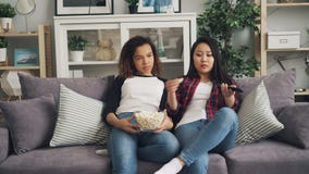 Οι τρυπημένες νέες γυναίκες προσέχουν τη TV μαζί στο σπίτι και τρώνε popcorn τη συνεδρίαση στον καναπέ στο καθιστικό Το ασιατικό φιλμ μικρού μήκους Οι τρυπημένες νέες γυναίκες προσέχουν τη TV μαζί στο σπίτι και τρώνε popcorn τη συνεδρίαση στον καναπέ στο καθιστικό Το ασιατικό φιλμ μικρού μήκους