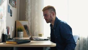Όμορφο νέο σπίτι freelancer με τα γυαλιά και την κίτρινη τρίχα που λειτουργούν στο σπίτι, χρησιμοποιώντας ένα lap-top Παίρνοντας φιλμ μικρού μήκους Όμορφο νέο σπίτι freelancer με τα γυαλιά και την κίτρινη τρίχα που λειτουργούν στο σπίτι, χρησιμοποιώντας ένα lap-top Παίρνοντας φιλμ μικρού μήκους