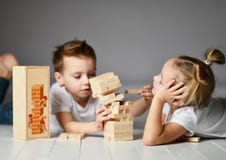Το αγόρι και το κορίτσι δύο παιδιών στις άσπρες μπλούζες βρίσκονται στο πάτωμα και παίζουν Jenga στοκ φωτογραφίες με δικαίωμα ελεύθερης χρήσης Το αγόρι και το κορίτσι δύο παιδιών στις άσπρες μπλούζες βρίσκονται στο πάτωμα και παίζουν Jenga στοκ φωτογραφίες με δικαίωμα ελεύθερης χρήσης