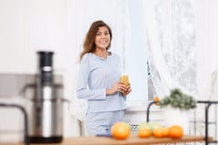 Το νέο κορίτσι brunette έντυσε στις ανοικτό μπλε στάσεις πυτζαμών με το ποτήρι του φρέσκου χυμού δίπλα στο παράθυρο στο φως στοκ εικόνα με δικαίωμα ελεύθερης χρήσης Το νέο κορίτσι brunette έντυσε στις ανοικτό μπλε στάσεις πυτζαμών με το ποτήρι του φρέσκου χυμού δίπλα στο παράθυρο στο φως στοκ εικόνα με δικαίωμα ελεύθερης χρήσης