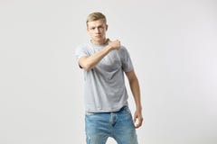 Агрессивный белокурый парень одетый в белой футболке и стойках джинсов на белой предпосылке в студии стоковое фото rf Агрессивный белокурый парень одетый в белой футболке и стойках джинсов на белой предпосылке в студии стоковое фото rf