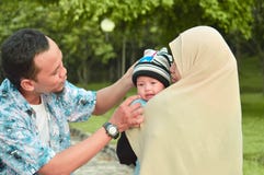 Азиатские мусульманские мать hijabi и прогулка отца через парк с сыном в прогулочной коляске пока его мама позаботить об ее todle стоковое изображение Азиатские мусульманские мать hijabi и прогулка отца через парк с сыном в прогулочной коляске пока его мама позаботить об ее todle стоковое изображение