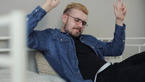 Всход образа жизни молодого привлекательного millenial человека со стильной стрижкой играя игру на смартфоне в белой кровати акции видеоматериалы Всход образа жизни молодого привлекательного millenial человека со стильной стрижкой играя игру на смартфоне в белой кровати акции видеоматериалы