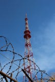 Высокая антенна радио ТВ со спутниковым сигналом за загородкой колючей проволоки против голубого неба стоковое фото Высокая антенна радио ТВ со спутниковым сигналом за загородкой колючей проволоки против голубого неба стоковое фото