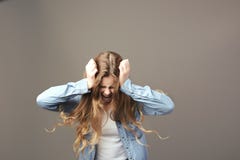 Грустная коричнев-с волосами девушка одетая в белых футболке и демикотоне держит ее руки на ее голове и окриках на серой предпосы стоковая фотография rf Грустная коричнев-с волосами девушка одетая в белых футболке и демикотоне держит ее руки на ее голове и окриках на серой предпосы стоковая фотография rf