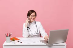 Женский доктор сидит на работе стола на компьютере с медицинским мобильным телефоном владением документа в изолированной больнице стоковое фото Женский доктор сидит на работе стола на компьютере с медицинским мобильным телефоном владением документа в изолированной больнице стоковое фото