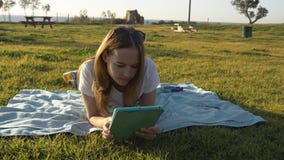 Женский используя планшет в парке с морем на горизонте стоковые изображения Женский используя планшет в парке с морем на горизонте стоковые изображения