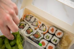 Женщина есть edamame, семг, surimi, огурец и авокадо Maki и внутренность - вне суши Калифорния с соевым соусом, замаринованным им стоковые изображения Женщина есть edamame, семг, surimi, огурец и авокадо Maki и внутренность - вне суши Калифорния с соевым соусом, замаринованным им стоковые изображения