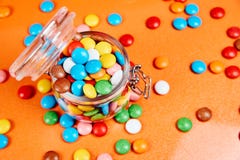 Красочные конфеты в стеклянном опарнике на красной предпосылке апельсинов стоковое изображение Красочные конфеты в стеклянном опарнике на красной предпосылке апельсинов стоковое изображение