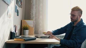 Красивый молодой домашний фрилансер со стеклами и желтыми волосами работая дома, используя ноутбук Пока получающ плохую новость о акции видеоматериалы Красивый молодой домашний фрилансер со стеклами и желтыми волосами работая дома, используя ноутбук Пока получающ плохую новость о акции видеоматериалы