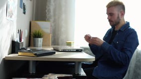 Молодой мужской домашний фрилансер со стеклами и желтыми волосами принимает стекла раскрывает и начинает использовать ноутбук Дом акции видеоматериалы Молодой мужской домашний фрилансер со стеклами и желтыми волосами принимает стекла раскрывает и начинает использовать ноутбук Дом акции видеоматериалы