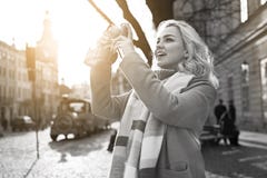 Молодая красивая жизнерадостная белокурая женщина принимая фото с ее винтажной камерой фильма на солнечный день на квадрат Rynok стоковое изображение rf Молодая красивая жизнерадостная белокурая женщина принимая фото с ее винтажной камерой фильма на солнечный день на квадрат Rynok стоковое изображение rf