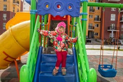 Маленькая девочка, тепло одетая, в играх шляпы и куртки на спортивной площадке со скольжениями и качаниями во дворе residentia стоковая фотография Маленькая девочка, тепло одетая, в играх шляпы и куртки на спортивной площадке со скольжениями и качаниями во дворе residentia стоковая фотография