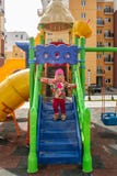 Маленькая девочка, тепло одетая, в играх шляпы и куртки на спортивной площадке со скольжениями и качаниями во дворе residentia стоковые фотографии rf Маленькая девочка, тепло одетая, в играх шляпы и куртки на спортивной площадке со скольжениями и качаниями во дворе residentia стоковые фотографии rf
