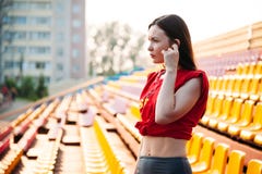 Сексуальная девушка спорта представляя на стадионе nad слушая музыку на наушниках Девушка фитнеса с диаграммой спорт в гетры и кр стоковое изображение rf Сексуальная девушка спорта представляя на стадионе nad слушая музыку на наушниках Девушка фитнеса с диаграммой спорт в гетры и кр стоковое изображение rf