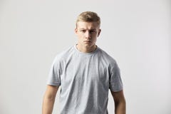 Серьезный белокурый парень одетый в белой футболке стоит на белой предпосылке в студии стоковая фотография Серьезный белокурый парень одетый в белой футболке стоит на белой предпосылке в студии стоковая фотография