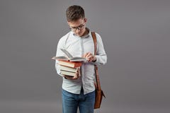 Умный парень в стеклах одетых в белой рубашке с коричневой сумкой читает книгу на серой предпосылке стоковая фотография Умный парень в стеклах одетых в белой рубашке с коричневой сумкой читает книгу на серой предпосылке стоковая фотография