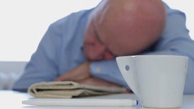 Уставший бизнесмен Napping дома с кофе и газетой на таблице стоковая фотография rf Уставший бизнесмен Napping дома с кофе и газетой на таблице стоковая фотография rf
