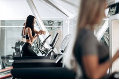 Тонкая темн-с волосами девушка одетая в черном sportswear для разработки на третбане в спортзале стоковое фото rf Тонкая темн-с волосами девушка одетая в черном sportswear для разработки на третбане в спортзале стоковое фото rf