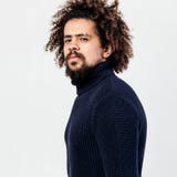 Темн-с волосами курчавый парень с бородой одетой в черном связанном turtleneck представляет в студии на белой предпосылке стоковая фотография Темн-с волосами курчавый парень с бородой одетой в черном связанном turtleneck представляет в студии на белой предпосылке стоковая фотография