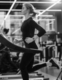 Черно-белое фото атлетической девушки одетой в черном sportswear бежать на третбане в современном спортзале стоковые изображения Черно-белое фото атлетической девушки одетой в черном sportswear бежать на третбане в современном спортзале стоковые изображения