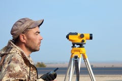 Работник с уровнем, построитель топографа с оборудованием геодезии близко к шоссе, с мобильным телефоном, усмехаясь стоковая фотография Работник с уровнем, построитель топографа с оборудованием геодезии близко к шоссе, с мобильным телефоном, усмехаясь стоковая фотография