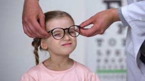 Óptico que pone los vidrios en niña y que hace su ayuda feliz, profesional almacen de metraje de vídeo Óptico que pone los vidrios en niña y que hace su ayuda feliz, profesional almacen de metraje de vídeo