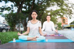 Övande yoga och meditation för kvinna på den matta nära lagun med pojkvännen royaltyfri bild Övande yoga och meditation för kvinna på den matta nära lagun med pojkvännen royaltyfri bild
