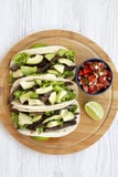 Över huvudet sikt, havretortillor med grillat nötkött, avokado, limefrukt och salsa på bambubräde Från över bästa sikt, lekmanna- royaltyfri foto Över huvudet sikt, havretortillor med grillat nötkött, avokado, limefrukt och salsa på bambubräde Från över bästa sikt, lekmanna- royaltyfri foto