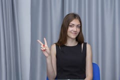 Ładna kobieta w białym koszulowym biurowym desktop przedstawień dwa palców szarość tle fotografia stock Ładna kobieta w białym koszulowym biurowym desktop przedstawień dwa palców szarość tle fotografia stock