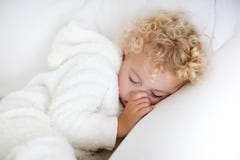 Śliczny blond kędzierzawy chłopiec dosypianie na białej leżance obrazy stock Śliczny blond kędzierzawy chłopiec dosypianie na białej leżance obrazy stock