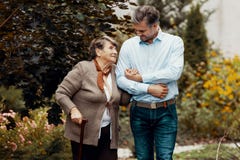 Άνδρας που υποστηρίζει την αδύνατη ανώτερη γυναίκα με το ραβδί περπατήματος στον κήπο στοκ εικόνες Άνδρας που υποστηρίζει την αδύνατη ανώτερη γυναίκα με το ραβδί περπατήματος στον κήπο στοκ εικόνες